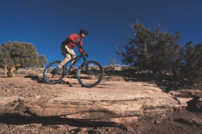 A man leads his dog off a ledge drop on the Horsethief Bench trail during a fall ride in the Kokopelli Trail System near Fruita, Colorado.