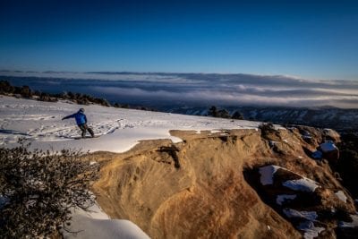 Master snowboarder Robbie Drake cuts a hard turn at the edge of a desert cliff on The Ribbon mountain bike trail above Grand Junction, Colorado.