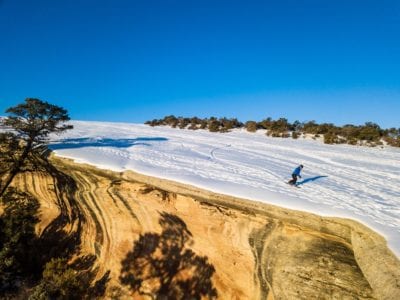 Snowboarding along the cliff edge of the desert mountain bike trail, The Ribbon, with a rare blanket of snow.